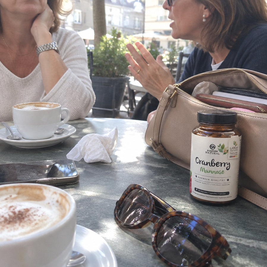 Café-Tisch mit Cappuccino, daneben Handtasche und eine Dose Surpresa Natural Cranberry Mannose